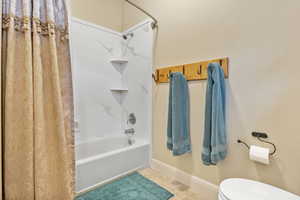 Bathroom with shower / bath combination with curtain, toilet, baseboards, and tile patterned floors