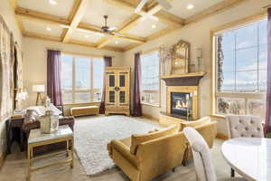 Living room featuring a glass covered fireplace, beamed ceiling, a ceiling fan, and coffered ceiling