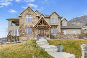 View of front facade with a front yard, a balcony, stone siding, and stucco siding