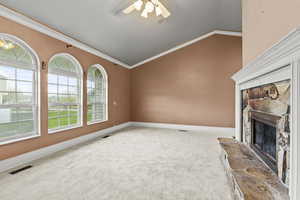Unfurnished living room featuring a stone fireplace, visible vents, vaulted ceiling, baseboards, and carpet flooring