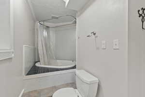 Bathroom featuring toilet, tiled shower / bath, tile patterned floors, and a textured ceiling