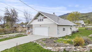View of side of home with a shingled roof, a mountain view, a chimney, concrete driveway, and a yard