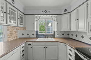 Kitchen with a sink, dishwasher, white cabinets, and glass insert cabinets