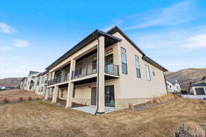 Back of property with stucco siding, a balcony, a patio, a lawn, and a mountain view