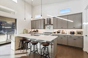 Kitchen featuring wall chimney range hood, a sink, gray cabinetry, and a high ceiling