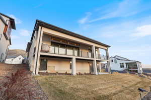 Rear view of house featuring a balcony, stucco siding, and a yard