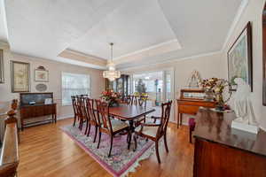 Dining room featuring crown molding, light wood-type flooring, a notable chandelier, and a raised ceiling
