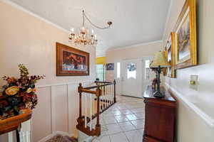 Foyer entrance with a wainscoted wall, a textured ceiling, crown molding, and an inviting chandelier