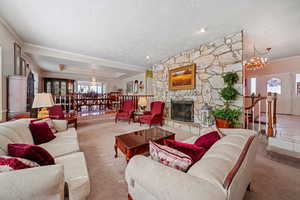 Carpeted living area with a textured ceiling, a chandelier, crown molding, a fireplace, and a tray ceiling