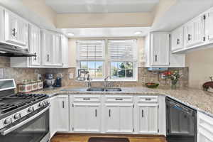 Kitchen featuring stainless steel gas stove, black dishwasher, under cabinet range hood, and white cabinetry