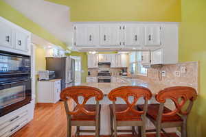 Kitchen with white cabinets, a peninsula, under cabinet range hood, black appliances, and backsplash