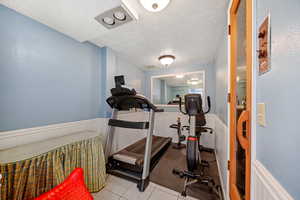 Exercise room with a wainscoted wall, tile patterned flooring, and a textured ceiling