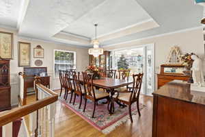 Dining space with light wood-type flooring, a chandelier, a raised ceiling, and crown molding