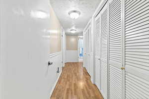 Hall featuring a textured ceiling, light wood finished floors, and a wainscoted wall