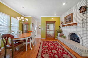 Dining space with a notable chandelier, a textured ceiling, a brick fireplace, light wood-style flooring, and ornamental molding