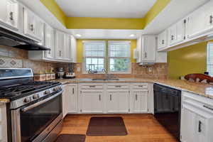 Kitchen with white cabinetry, under cabinet range hood, gas stove, a sink, and black dishwasher
