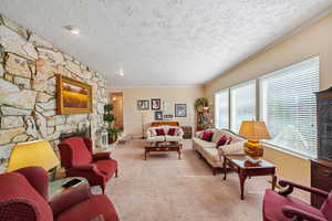 Living room featuring a stone fireplace, crown molding, carpet floors, and a textured ceiling