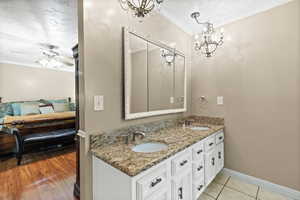 Ensuite bathroom featuring crown molding, double vanity, a chandelier, and a ceiling fan