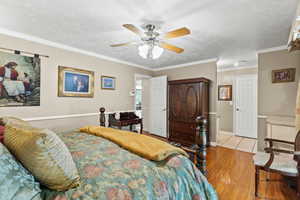 Bedroom featuring wood finished floors, ornamental molding, a ceiling fan, and a textured ceiling