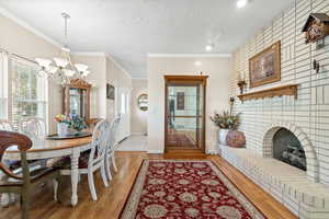 Dining space with a chandelier, light wood-type flooring, a textured ceiling, a brick fireplace, and crown molding