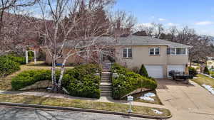 View of front of property with stairs, a garage, a chimney, brick siding, and driveway