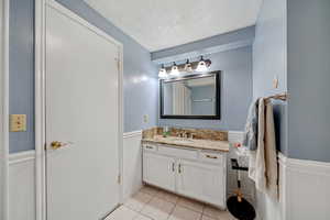 Bathroom featuring a wainscoted wall, a textured ceiling, tile patterned flooring, and vanity