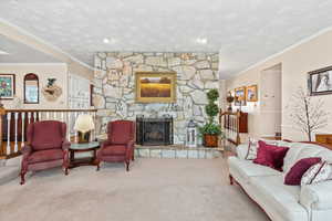 Carpeted living area featuring a fireplace, ornamental molding, and a textured ceiling