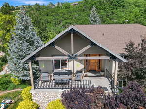 View of front of house with an outdoor living space, stucco siding, a patio area, roof with shingles, and a wooded view