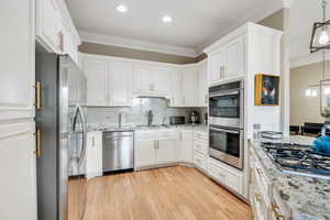 Kitchen featuring ornamental molding, appliances with stainless steel finishes, white cabinetry, a sink, and light wood-style floors