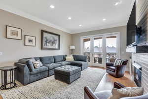 Living area with crown molding, wood finished floors, a glass covered fireplace, baseboards, and recessed lighting