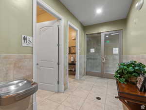 Bathroom with french doors, tile patterned flooring, a wainscoted wall, and tile walls