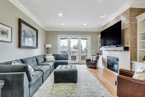 Living area featuring recessed lighting, light wood-style flooring, a glass covered fireplace, and crown molding