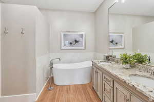 Bathroom with double vanity, a sink, a freestanding tub, and wood finished floors