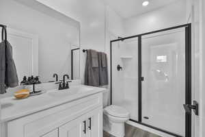 Full bathroom with toilet, vanity, a stall shower, and wood finished floors