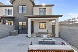 Rear view of house with stucco siding, a fenced backyard, central AC unit, outdoor lounge area, and a patio area