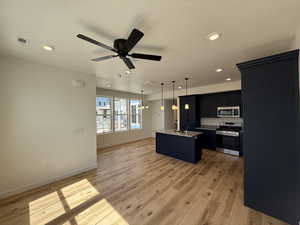 Kitchen with dark cabinets, open floor plan, a center island with sink, light wood-style floors, and appliances with stainless steel finishes