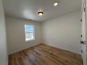 Unfurnished room featuring light wood finished floors, visible vents, baseboards, and a textured ceiling