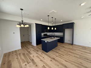 Kitchen with an island with sink, light wood-style flooring, a textured ceiling, appliances with stainless steel finishes, and a sink