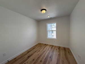 Unfurnished room with visible vents, light wood-style flooring, baseboards, and a textured ceiling