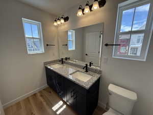 Full bath with baseboards, a sink, toilet, and wood finished floors