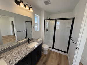 Bathroom with visible vents, toilet, vanity, wood finished floors, and a stall shower