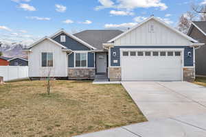 View of front of home featuring stone siding, fence, an attached garage, concrete driveway, and board and batten siding