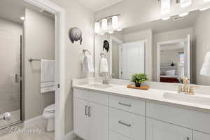 Ensuite bathroom with double vanity, visible vents, a shower stall, and a sink