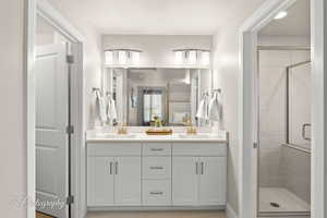 Bathroom featuring double vanity, connected bathroom, a stall shower, and a sink