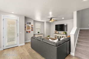 Living area featuring light wood-type flooring, stairway, baseboards, and a ceiling fan
