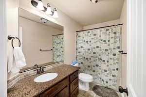 Bathroom with toilet, vanity, and curtained shower