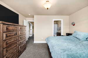 Bedroom with baseboards, a textured ceiling, dark carpet, and ensuite bathroom