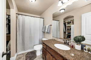 Bathroom featuring a spacious closet, toilet, vanity, and curtained shower