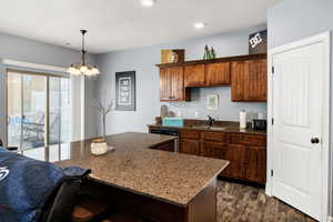 Kitchen with a sink, a chandelier, pendant lighting, dark wood finished floors, and dark stone countertops