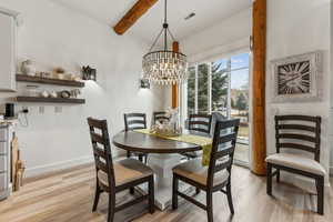 Dining room with light wood-type flooring, an inviting chandelier, baseboards, beamed ceiling, and visible vents